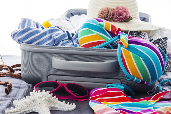 Colorful bikini and clothes in luggage on the bed